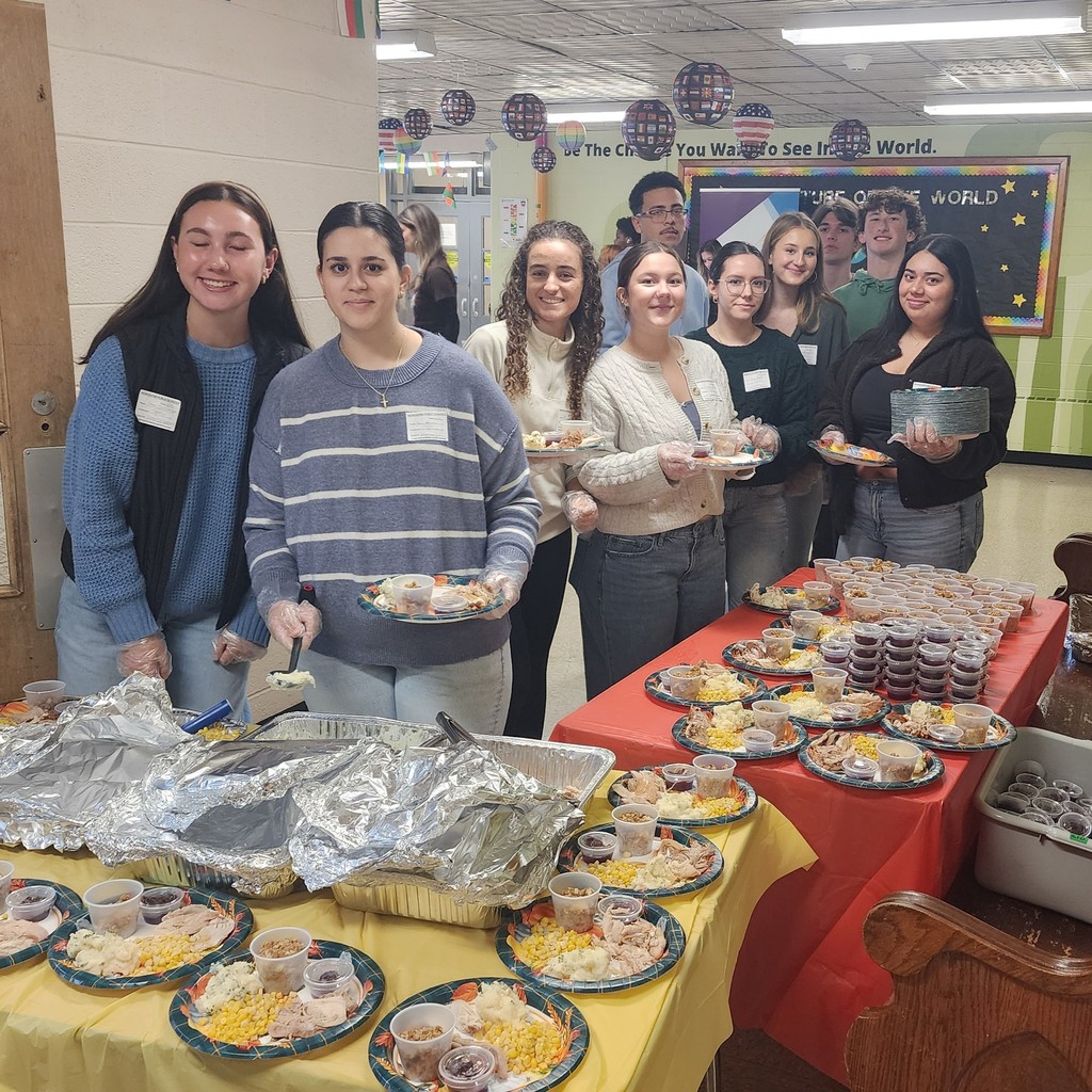 A group of people serve food from a table, smiling at the camera.