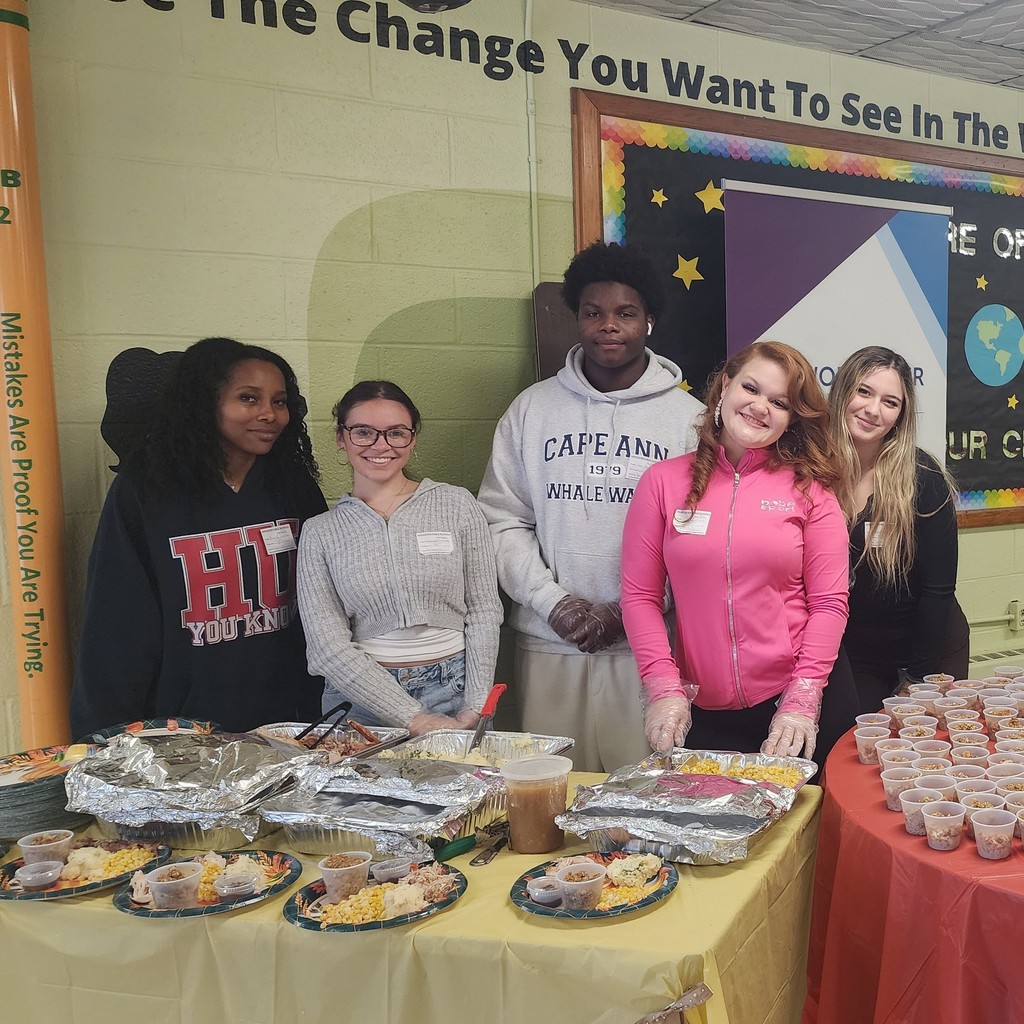 A group of people stand behind a table laden with food, smiling at the camera.