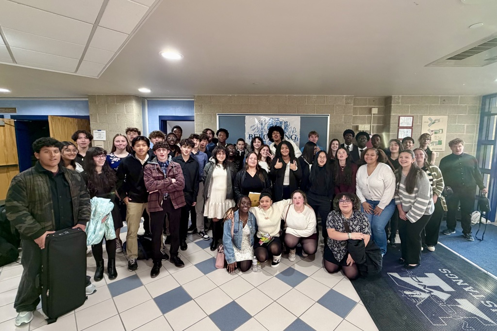 A large group of diverse students pose together in a school hallway.