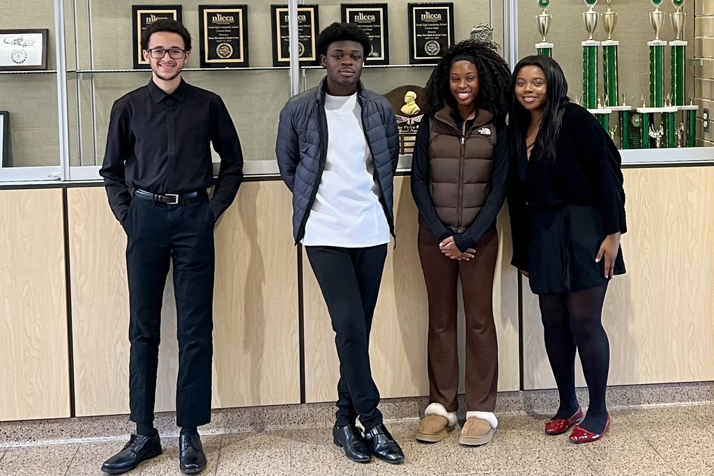 Four young adults stand together, smiling, in front of a display case.