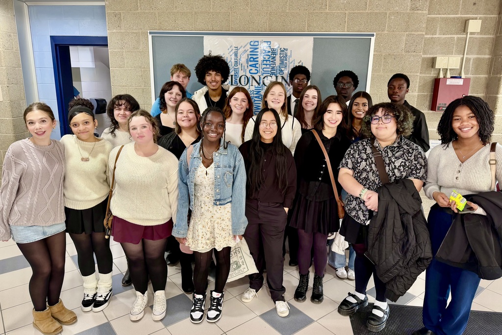 A diverse group of students poses for a photo in a school hallway.
