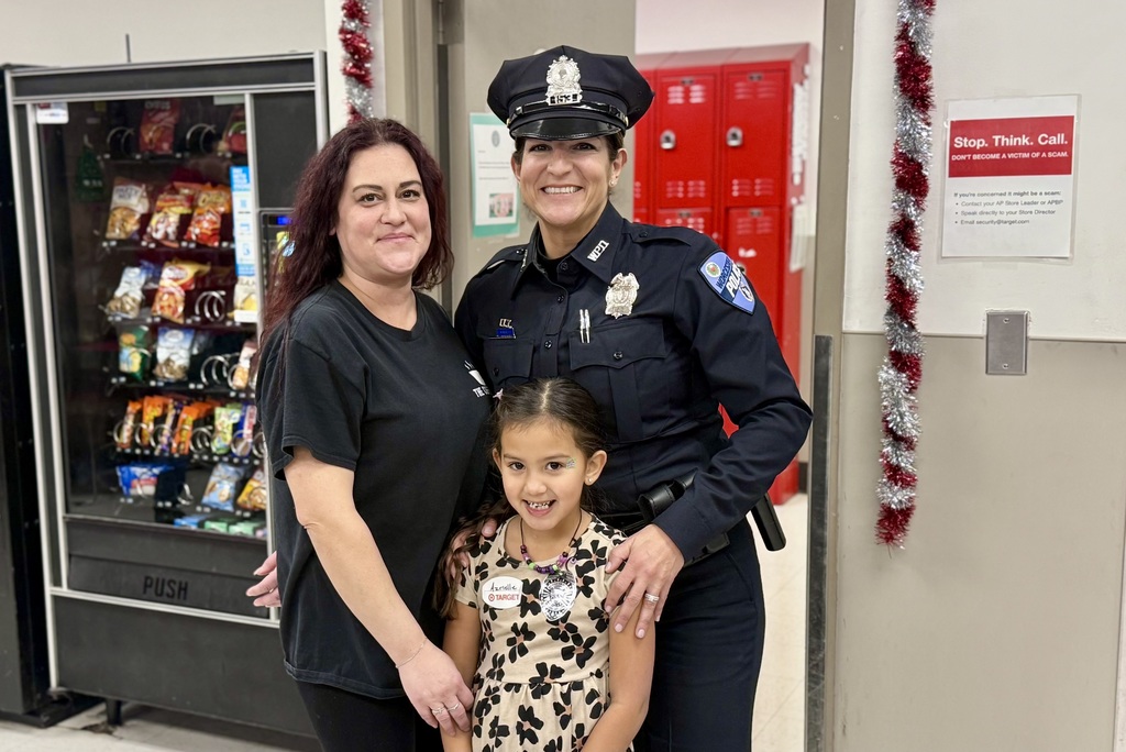 A police officer poses with a woman and a young girl in a store setting.