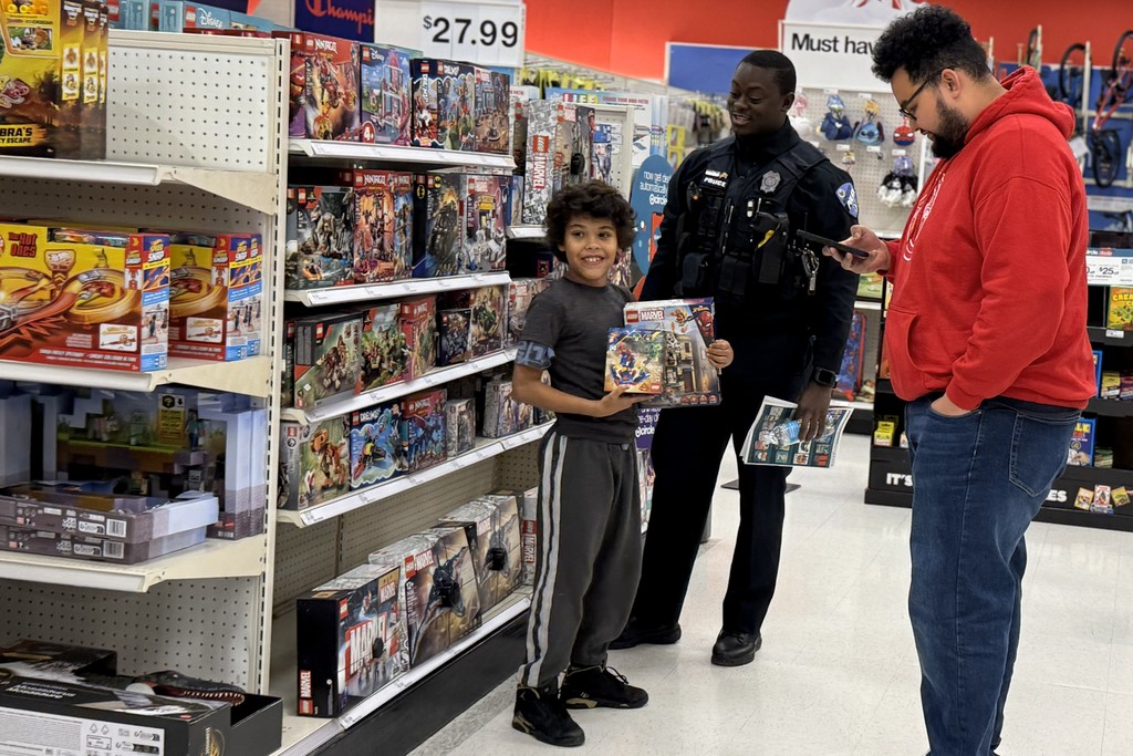 A young boy smiles, holding a LEGO Marvel set in a store aisle.