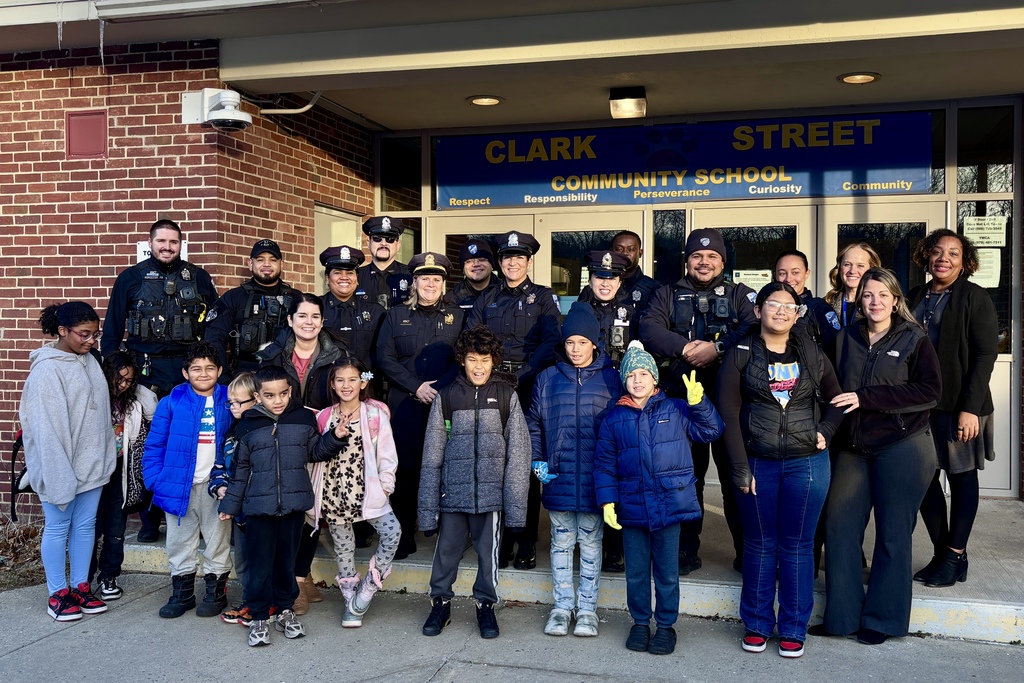 A group of police officers and children pose in front of a school building.