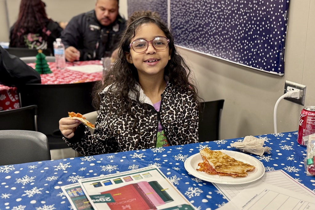 A child writes on a paper with a police officer, both at a table with a festive blue tablecloth.