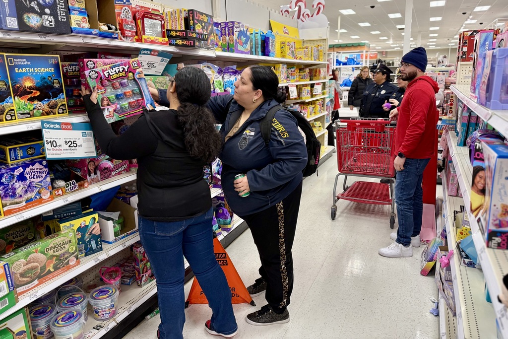 Two shoppers browse toys in a brightly lit store aisle, examining a colorful box.