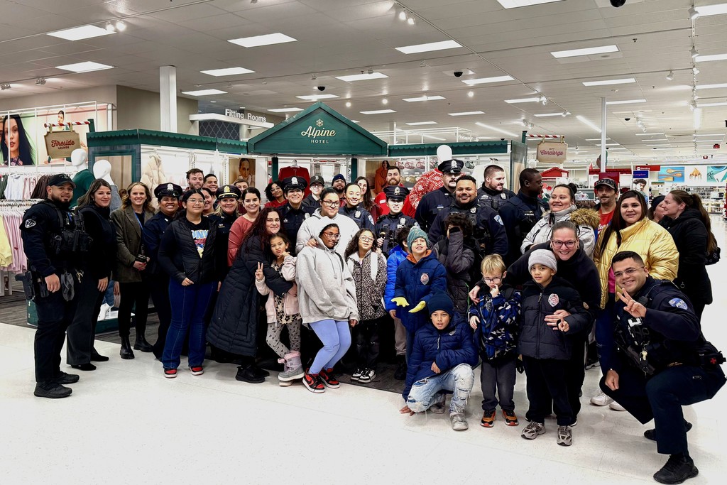 A large group of people, including police officers and children, pose for a photo inside a store.