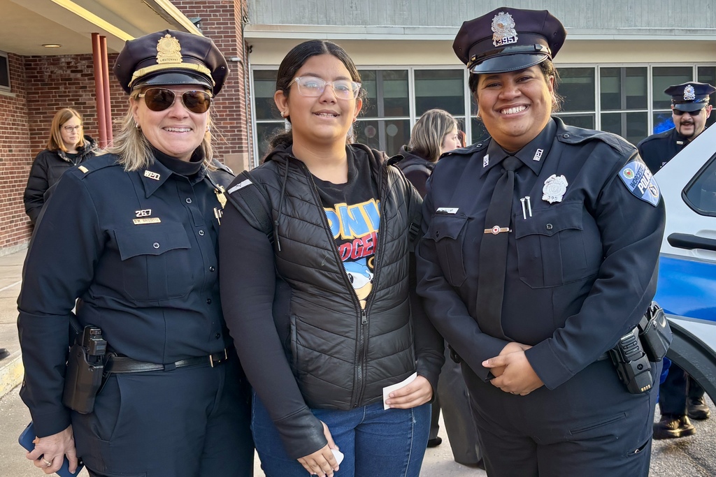 Two police officers pose with a smiling young person outdoors.