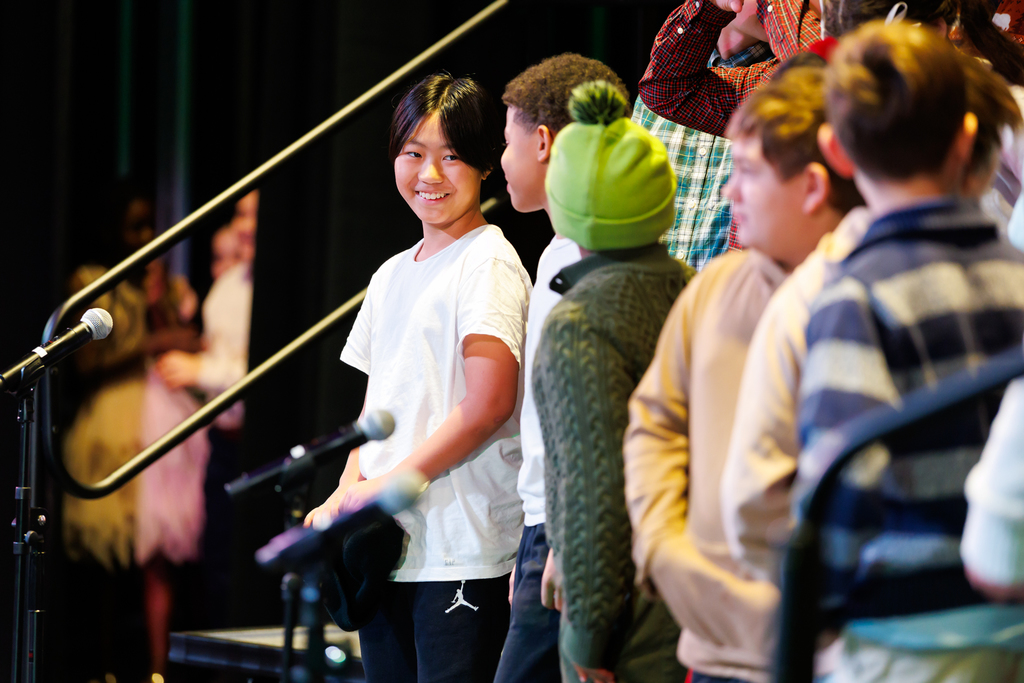 A young student smiles at nearby classmates during a holiday concert.