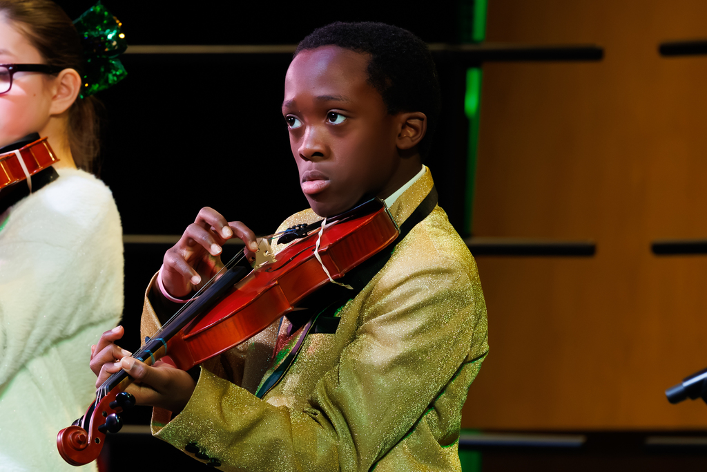A young student dressed in a green suit focuses while playing the violin.
