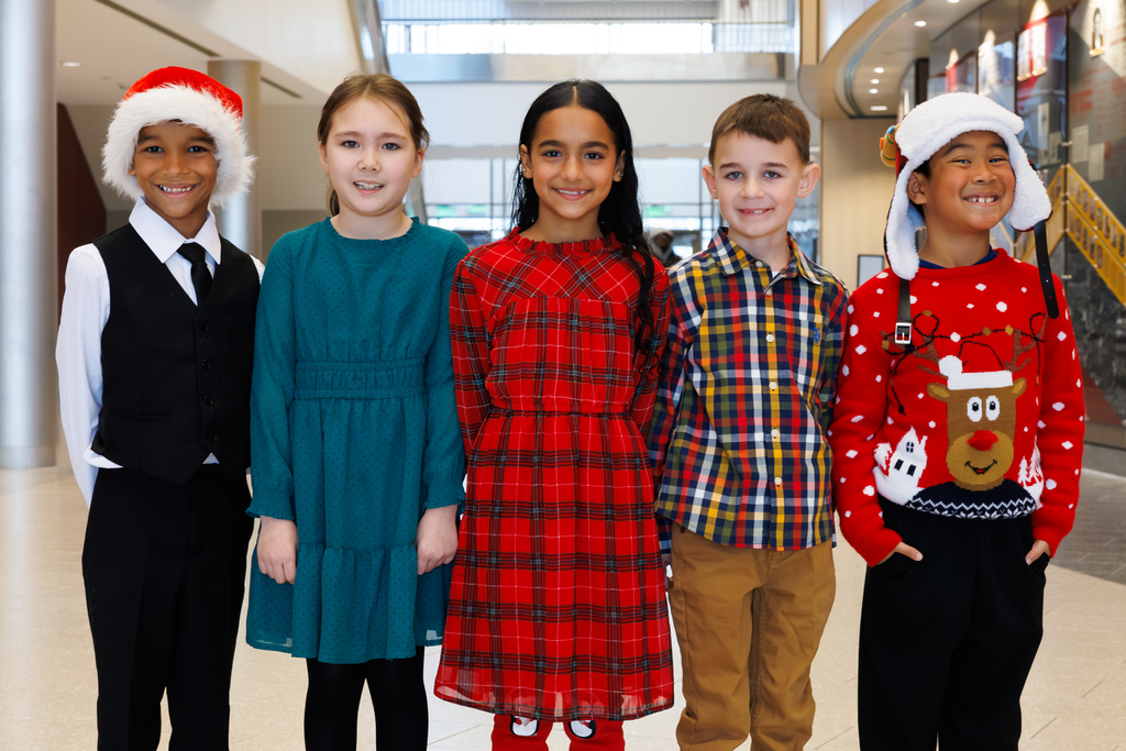 Five young students, dressed in holiday colors of green, red and blue, stand together and smile.