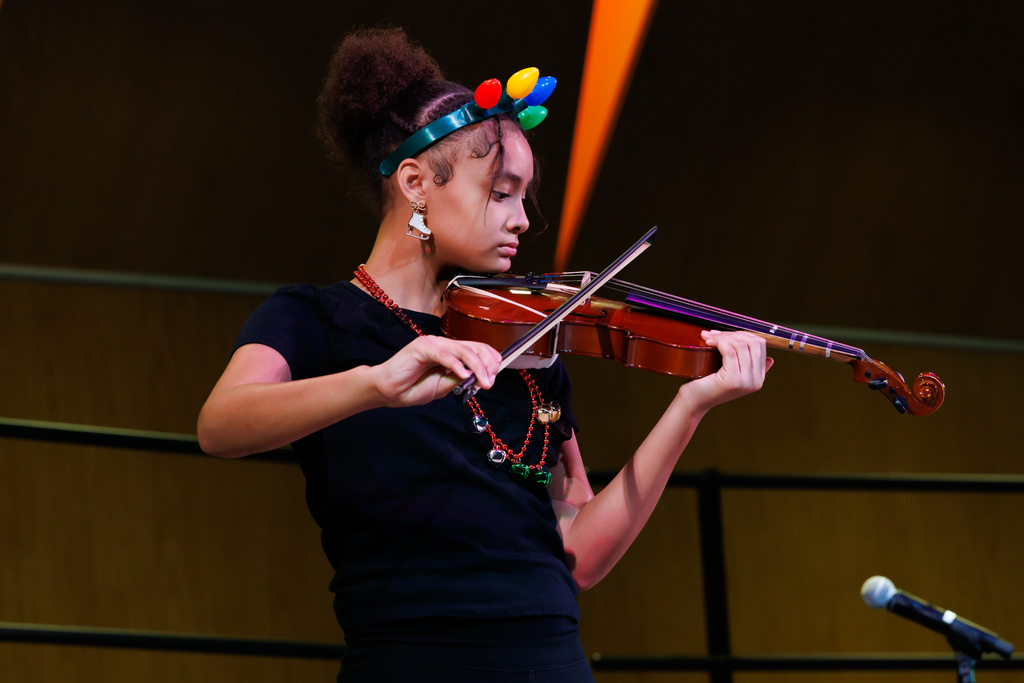 A student plays the violin while wearing a christmas light headband.
