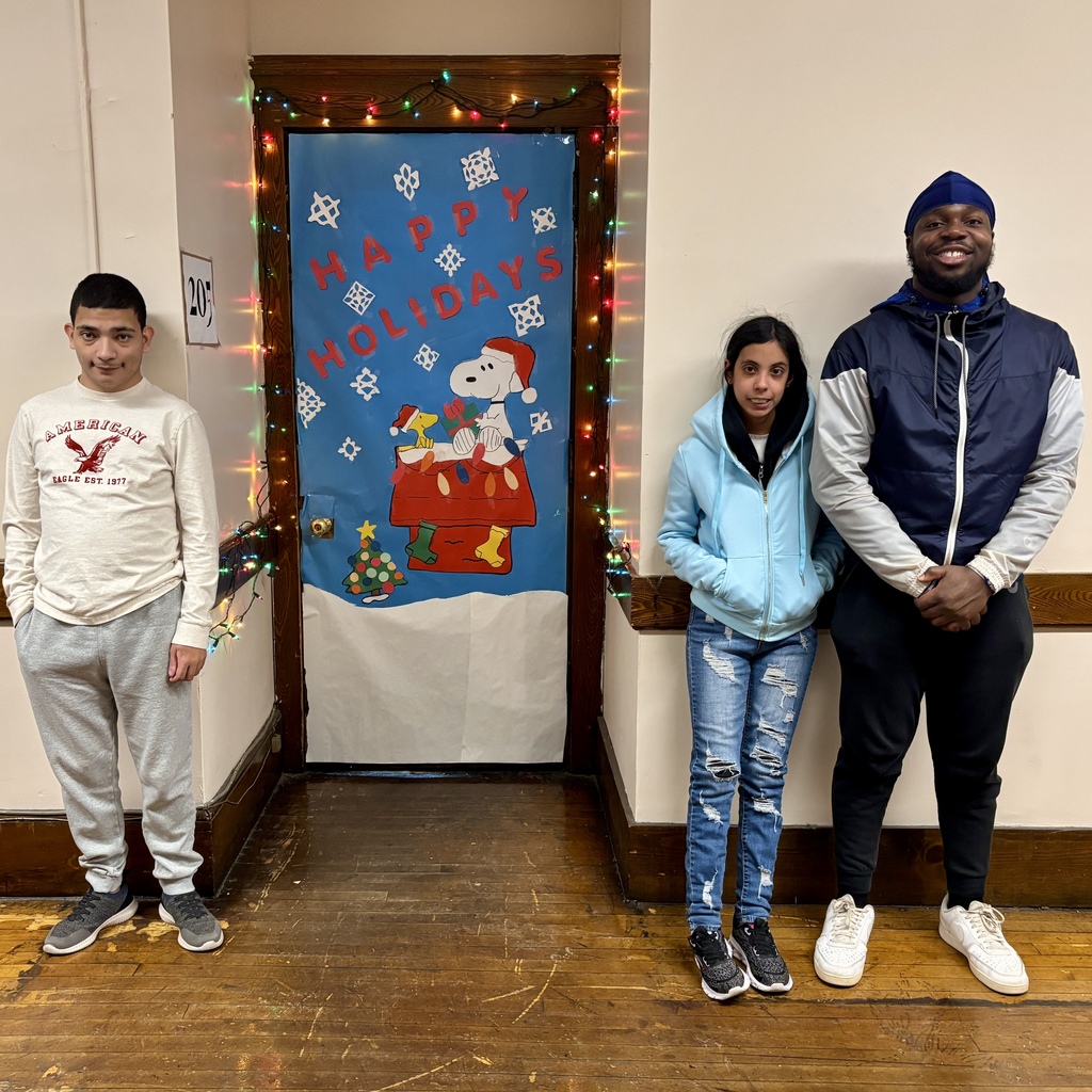 Three young people stand in a hallway next to a door decorated with Snoopy and holiday lights.