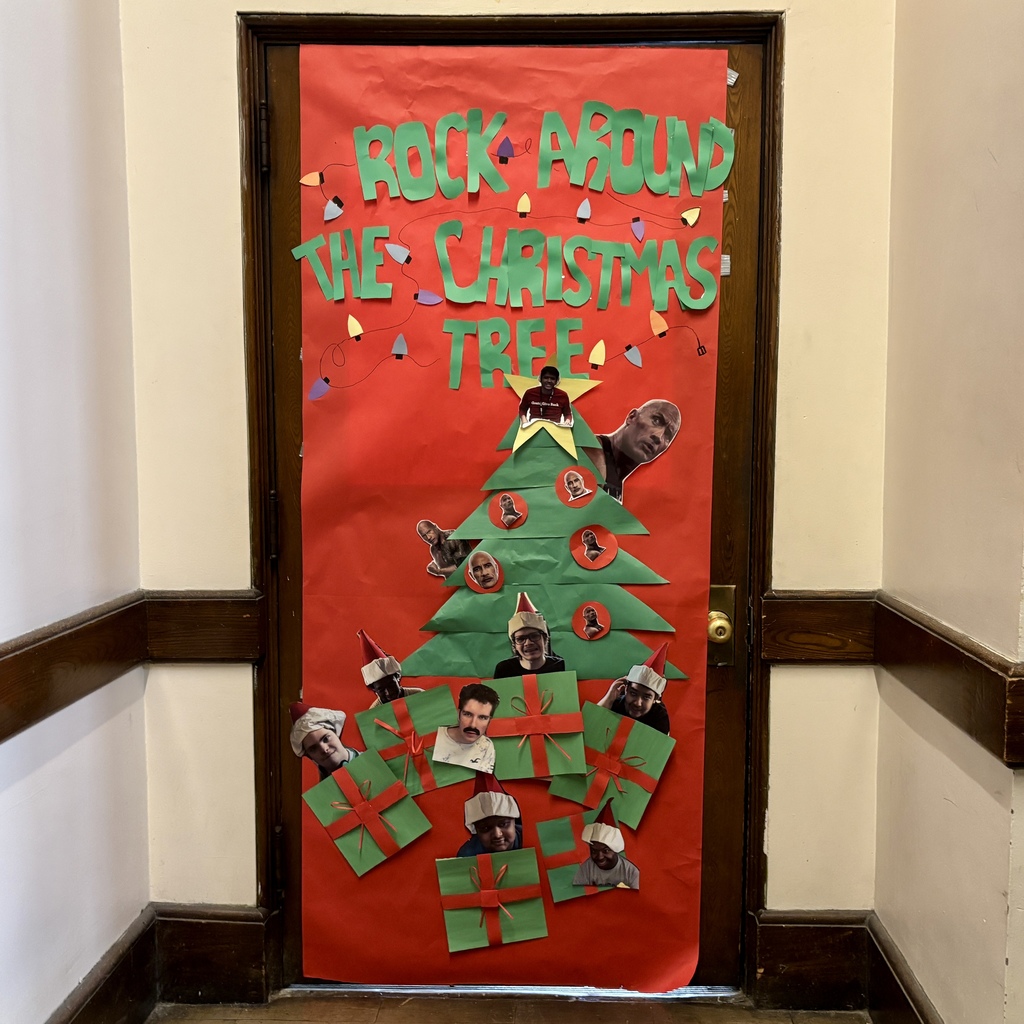 A red door decorated for Christmas with a large paper Christmas tree and the text 'ROCK AROUND THE CHRISTMAS TREE'.