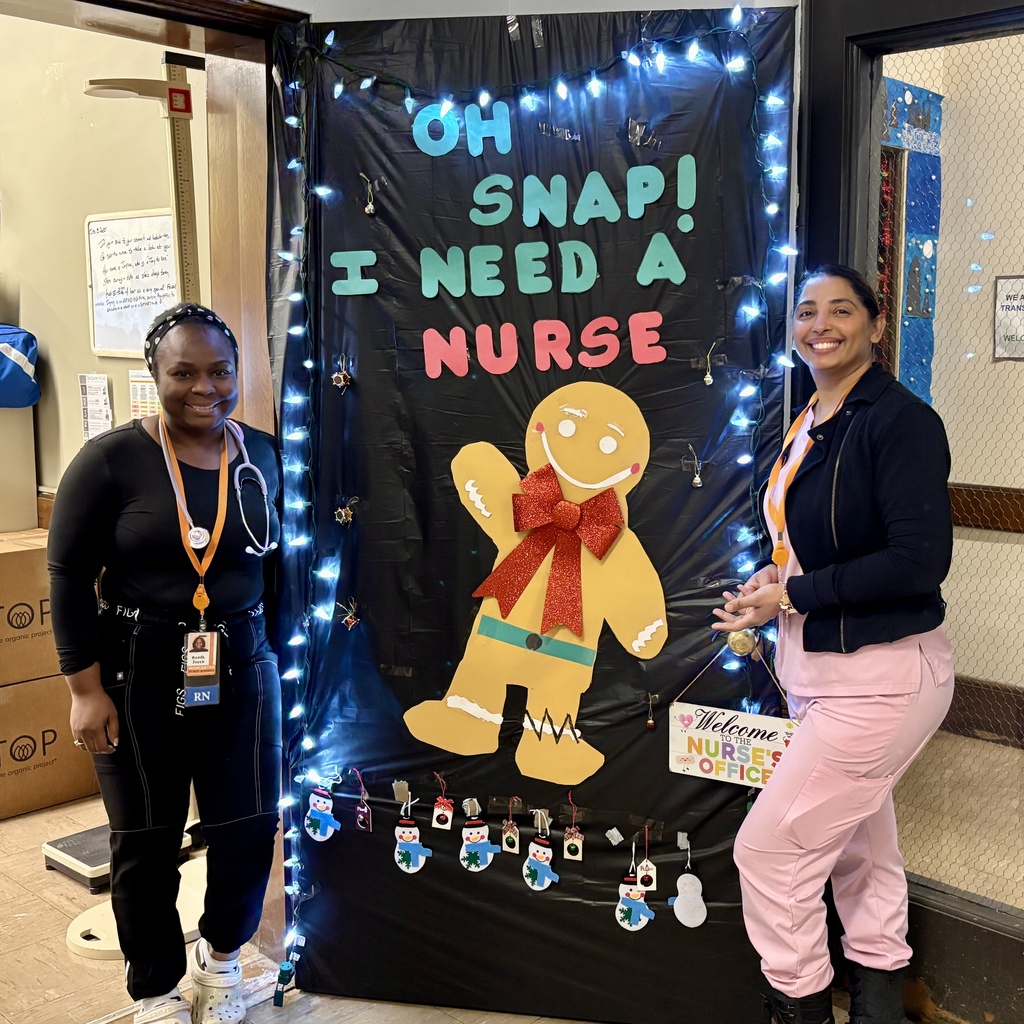 Two nurses smile in front of a festive black backdrop decorated with a gingerbread man and holiday lights.