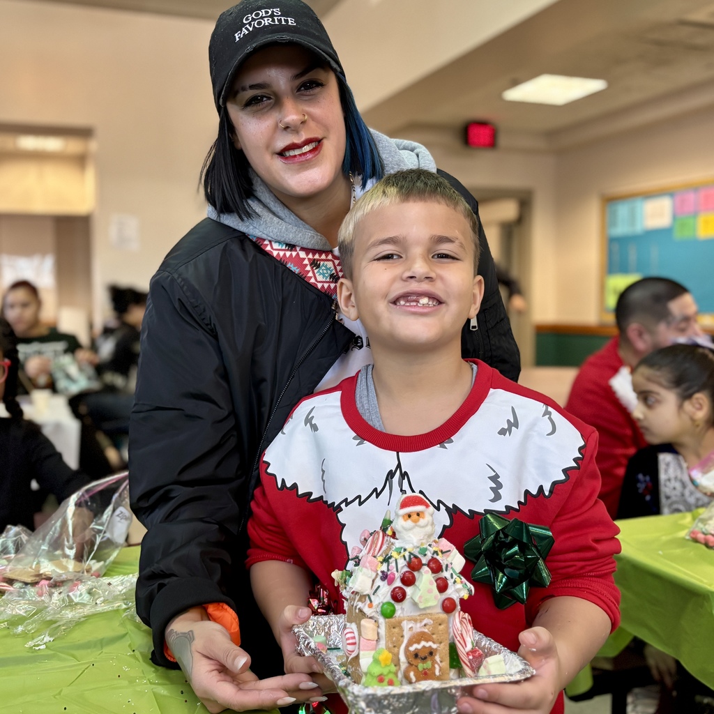 A woman and a child proudly display a decorated gingerbread house.