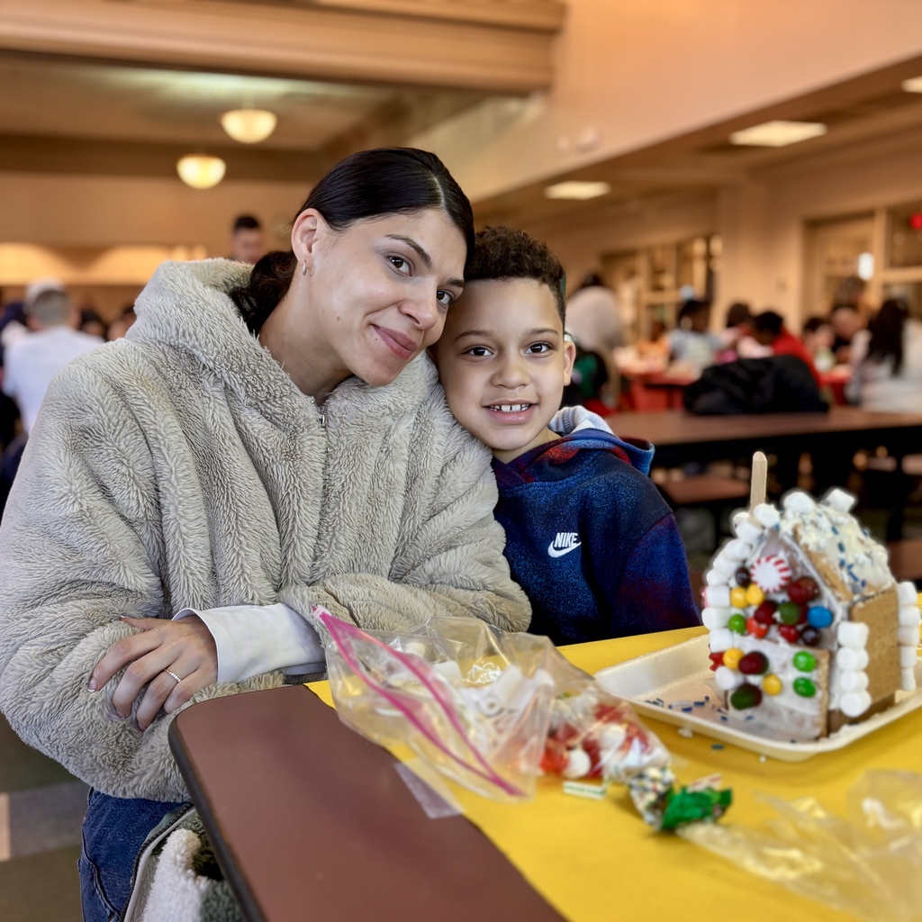 A woman and a young boy smile while sitting at a table with a decorated gingerbread house.