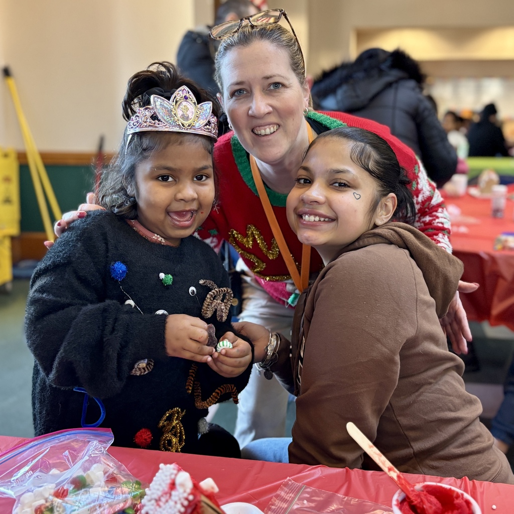 A woman smiles with two young girls, one wearing a tiara, at a festive event.