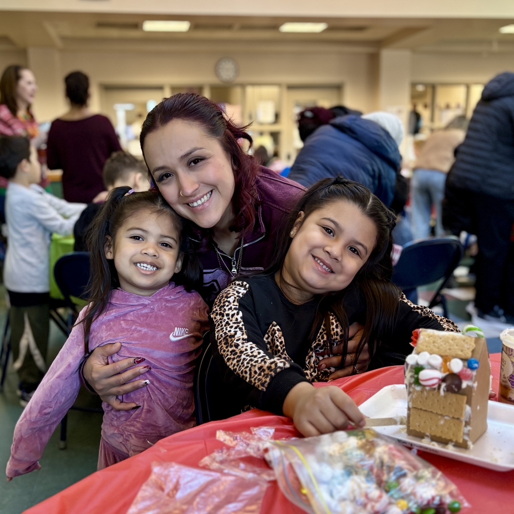 A woman smiles with two young girls while decorating a gingerbread house.