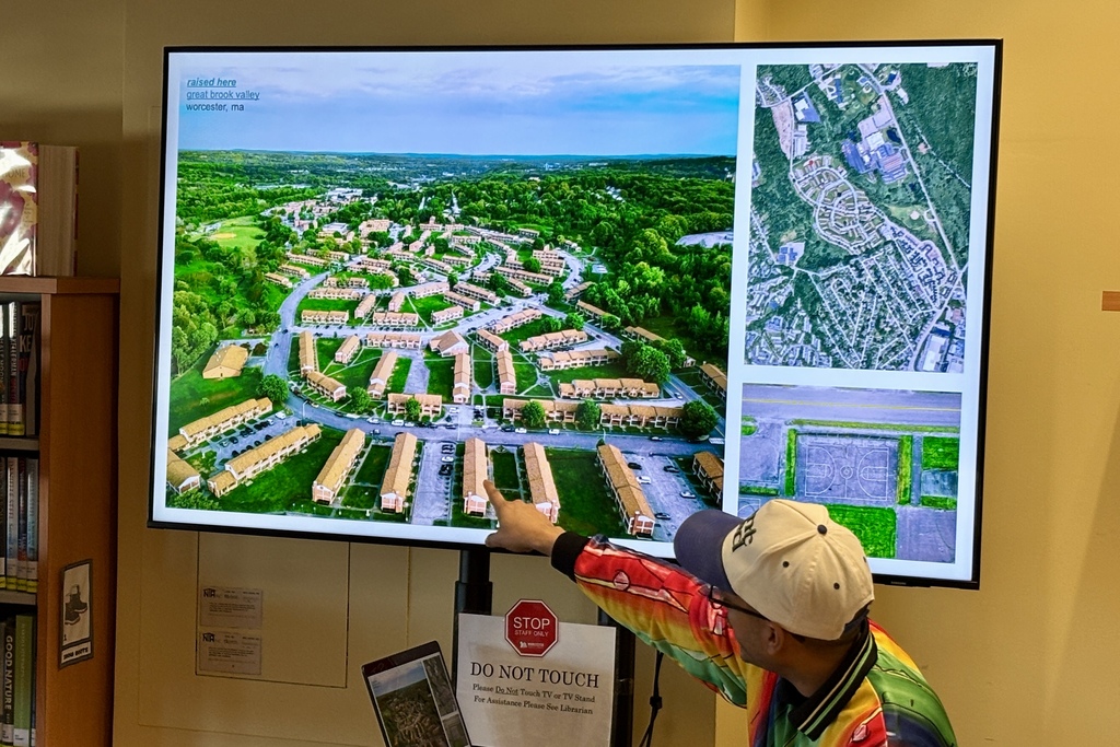 A person points at an aerial view of a residential area labeled 'great brook valley, worcester, ma' on a large screen.