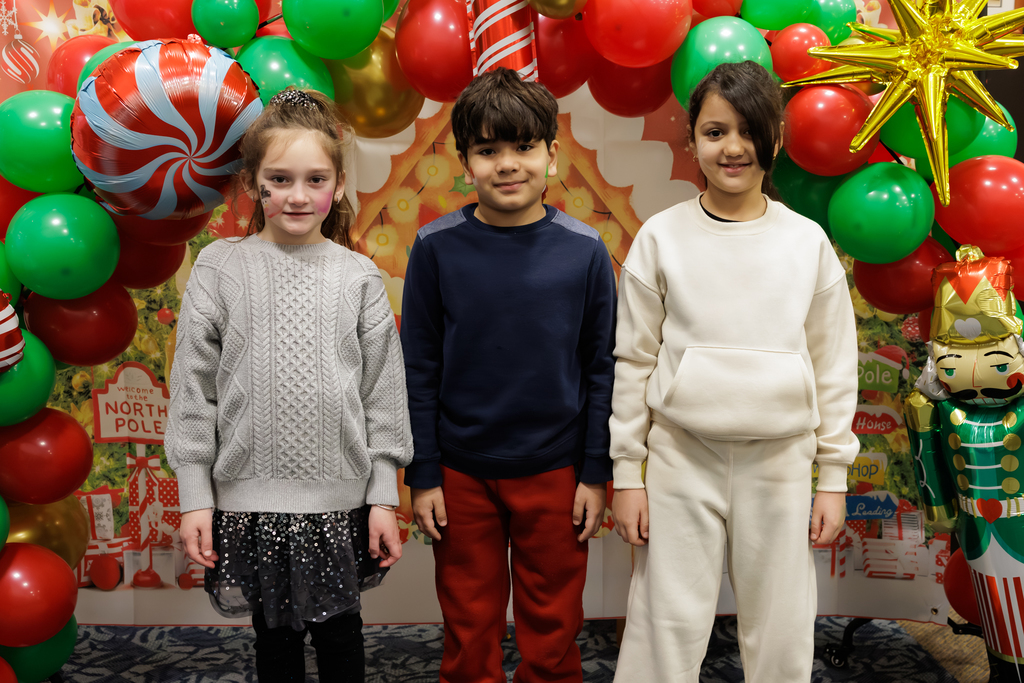Three students stand in front of a holiday themed balloon arch.