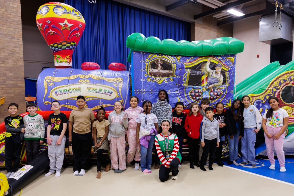 A class of students stand in front of a train themed bounce house.