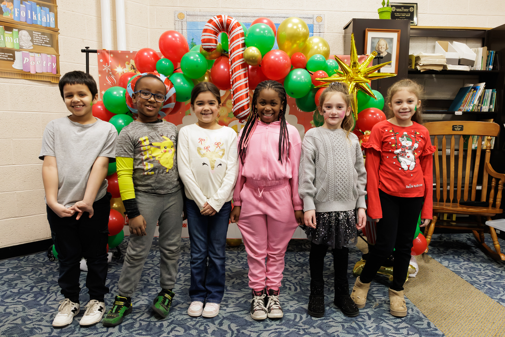 Six students stand in front of a holiday themed balloon arch.