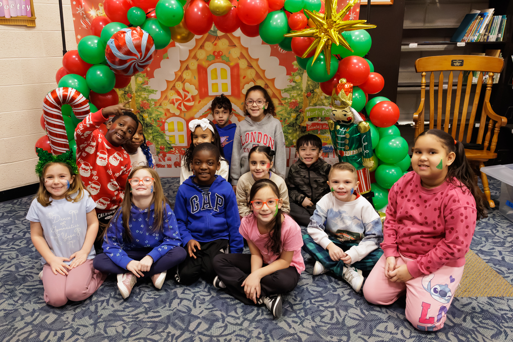 A large group of students stand in front of a holiday themed balloon arch.