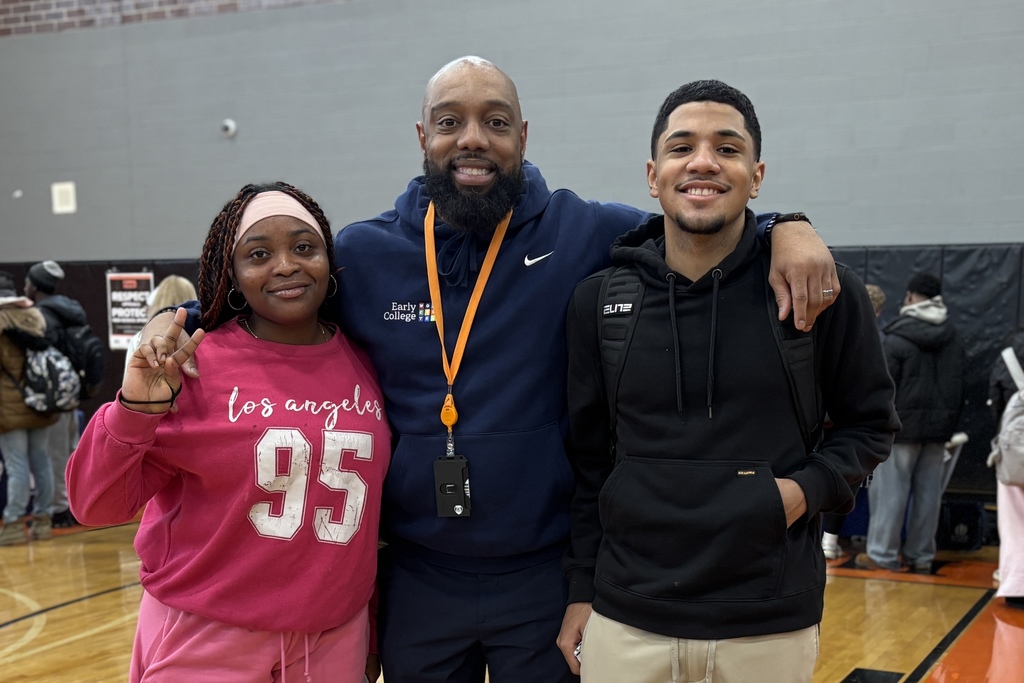 A smiling man with a beard stands between a young woman and a young man in a gymnasium.