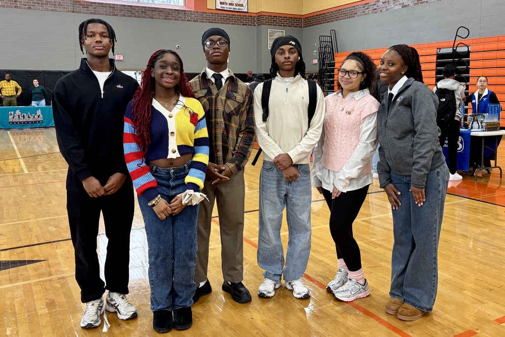 Six young people stand together in a gymnasium, posing for a photo.