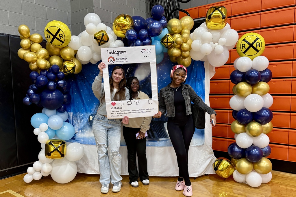 Three young women pose for a photo in front of a balloon arch and a backdrop, holding an Instagram-style frame.