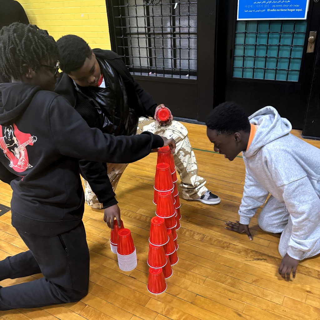 Three young people are stacking red cups in a gym.