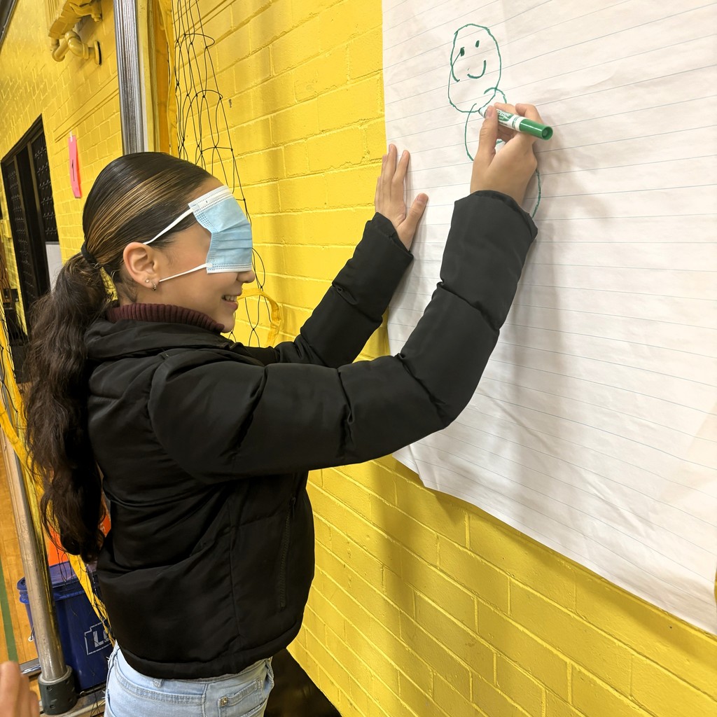 A girl wearing a face mask over her eyes draws a figure on a large sheet of paper.