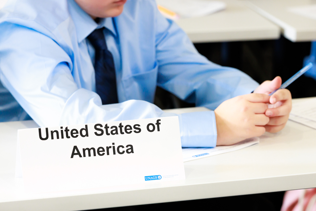A student looks at their paper while sitting behind a United States of America nameplate during a Model UN simulation.