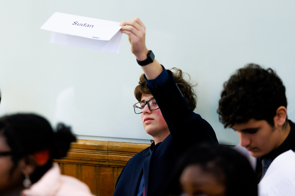 A high school student holds up their country nameplate to cast their vote in a Model UN simulation.