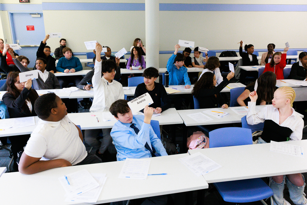 Middle school students hold up their country nameplate to cast their vote in a Model UN simulation.