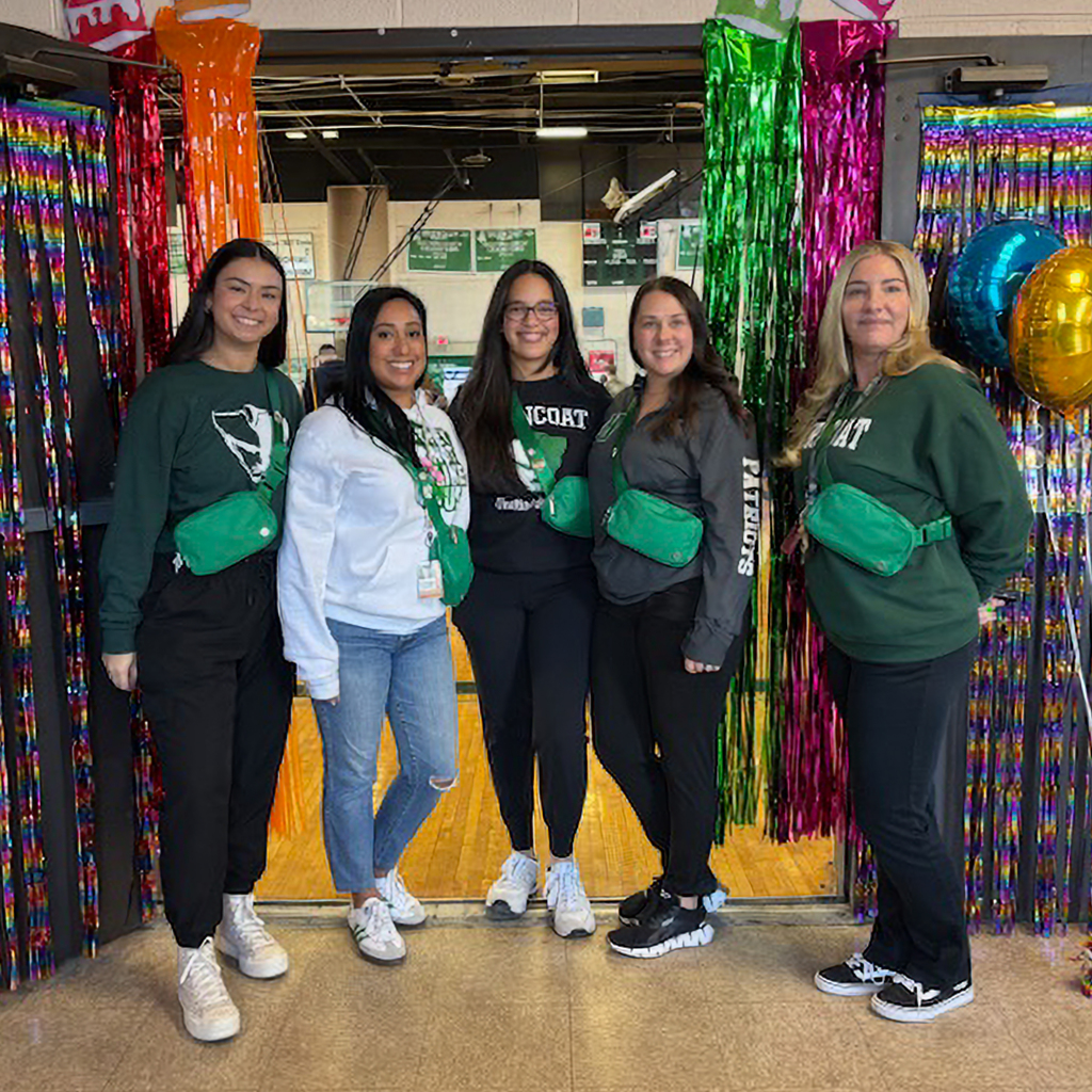 Five smiling individuals stand together in front of a backdrop of colorful streamers and balloons.