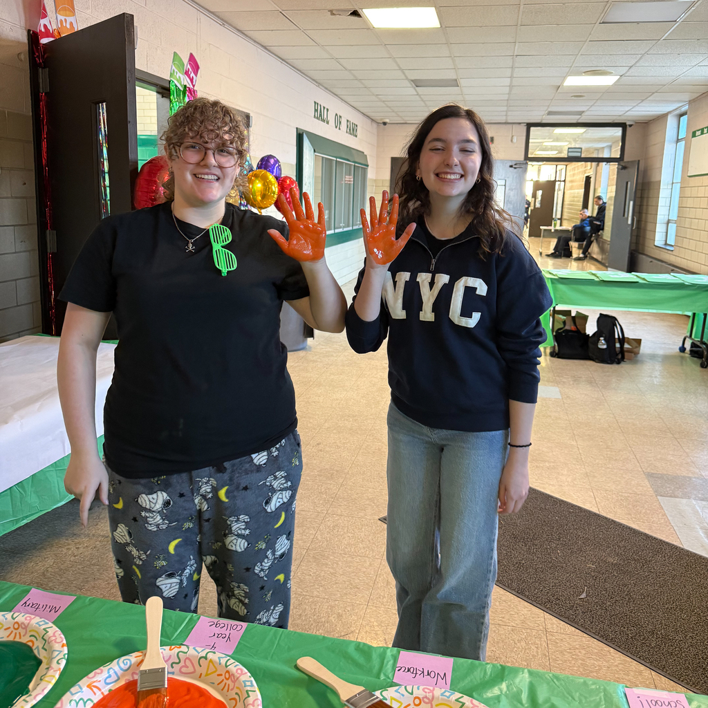 Two smiling young people show their hands painted orange at a table with art supplies.