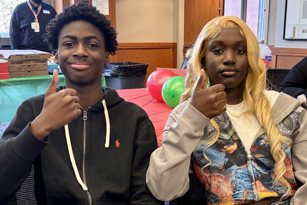 Two young people give a thumbs up, smiling at the camera.