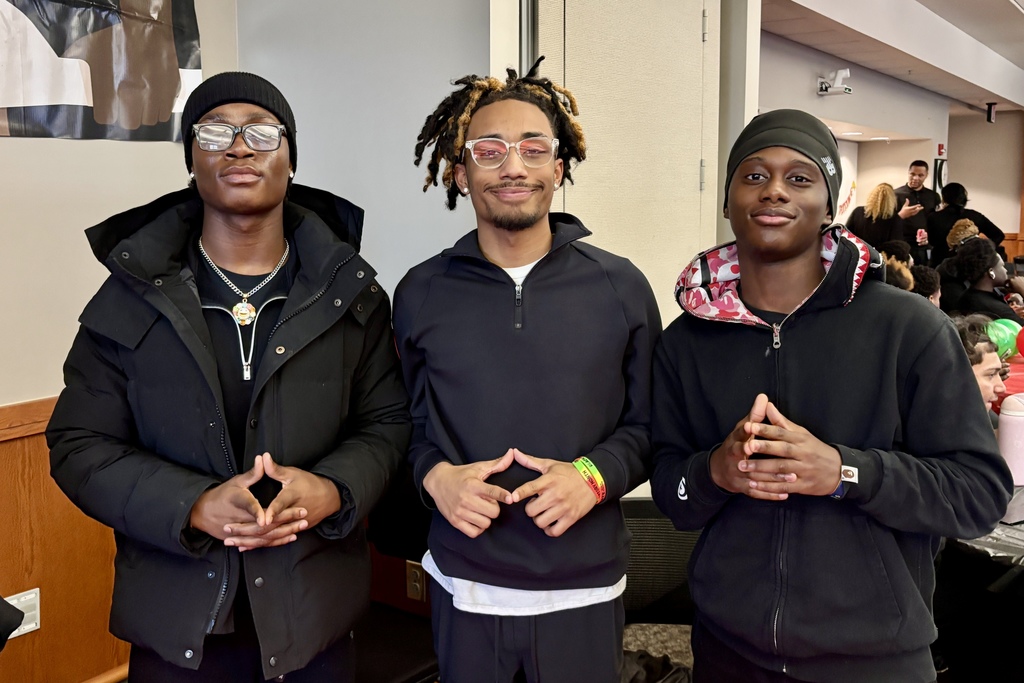 Three young men stand together, posing for a photo indoors.
