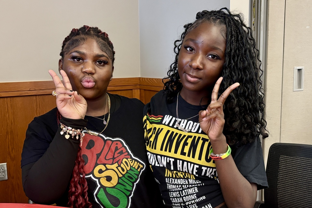 Two young women pose for a photo, both making peace signs with their hands.