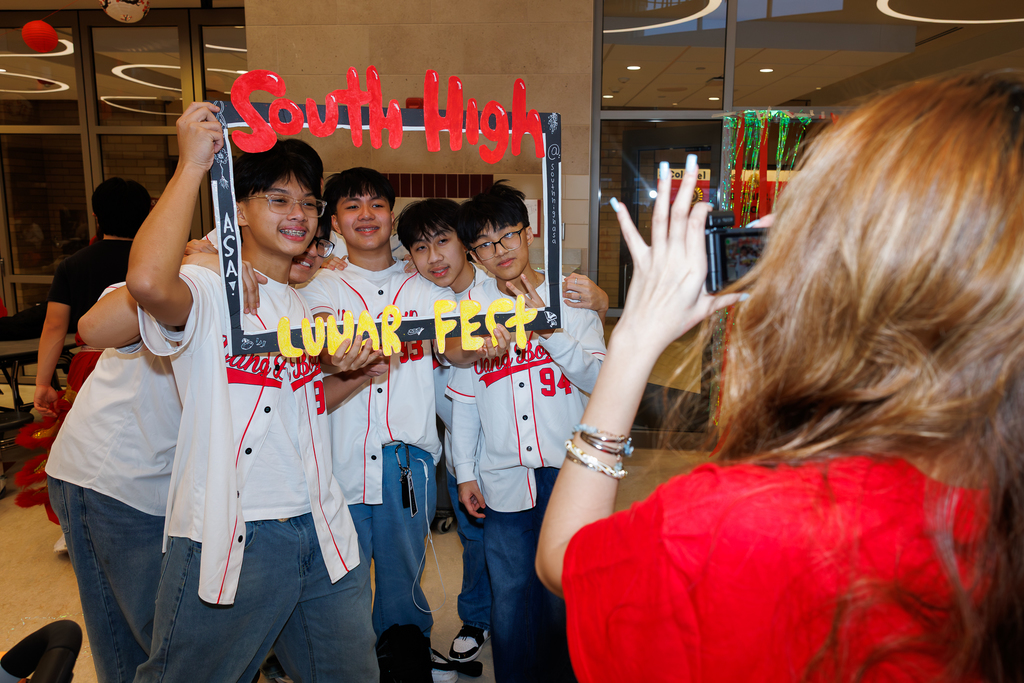 A group of students holding a frame that says "South High Lunar Fest" have their photo taken by another student,