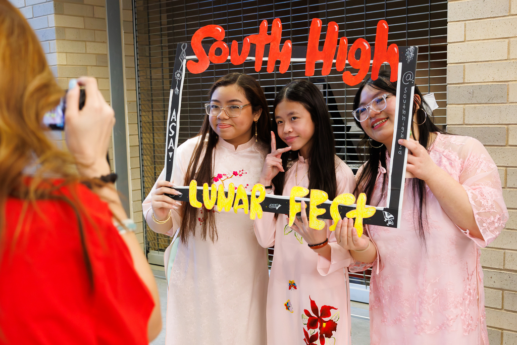 Three students in traditional cultural clothing take a photo holding a frame that says "South High Lunar Fest."