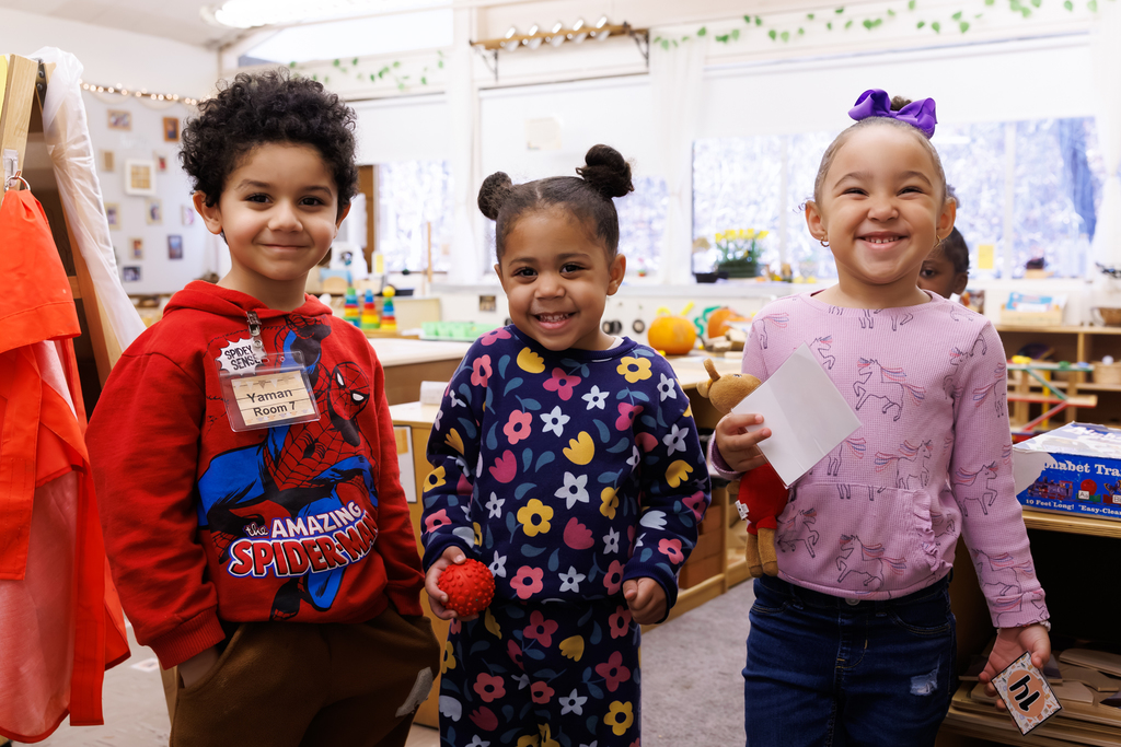 Three preschool-age children smile in a classroom