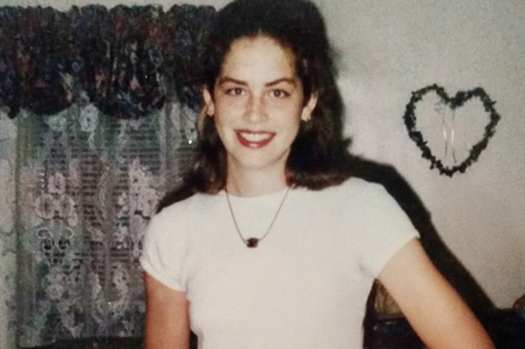 A young woman with dark hair smiles, wearing a white t-shirt and a necklace.