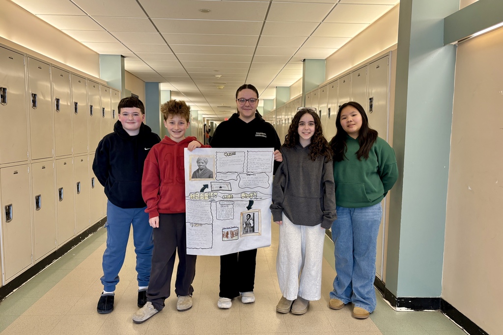 Five students stand in a school hallway, presenting a poster about Harriet Tubman.
