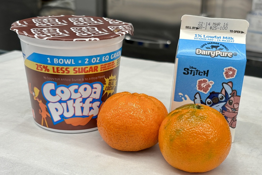 A single-serving cup of Cocoa Puffs cereal, two tangerines, and a carton of DairyPure 1% lowfat milk.