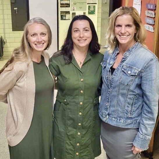 Three women smile for a photo, standing close together indoors.