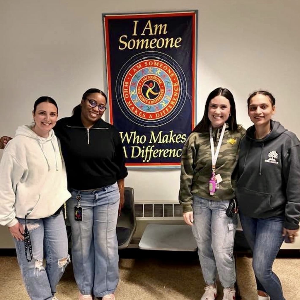 Four women stand together in front of a banner that reads 'I Am Someone Who Makes A Difference'.