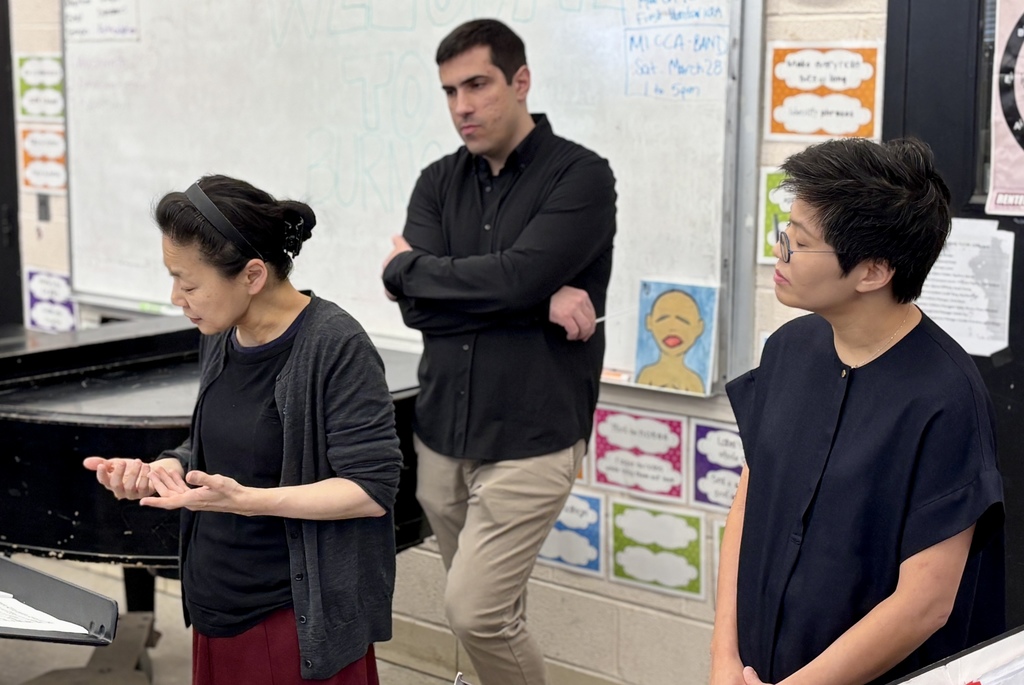 Three people stand in front of a whiteboard in a classroom setting.